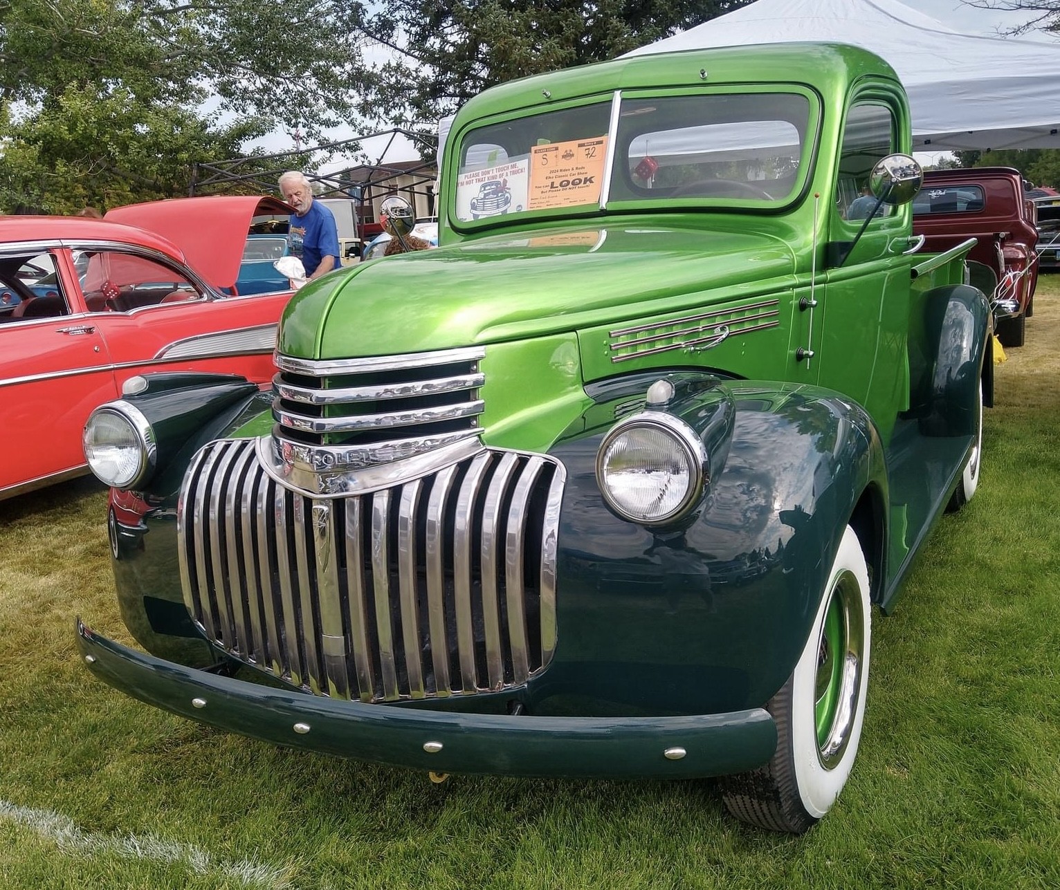 A green truck parked in the grass next to other cars.